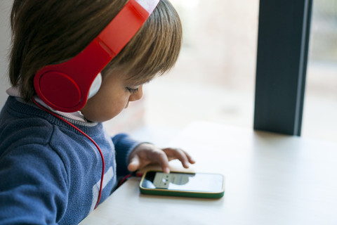 Kleiner Junge hört mit Kopfhörern die Musik seines Smartphones, lizenzfreies Stockfoto