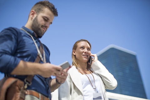 Junger Mann und Frau benutzen Mobiltelefone im Freien, lizenzfreies Stockfoto