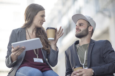 Young man and woman with tablet and coffee to go talking outdoors - ZEF12487