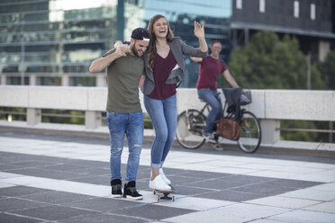 Junger Mann unterstützt lachende Freundin auf Skateboard - ZEF12492