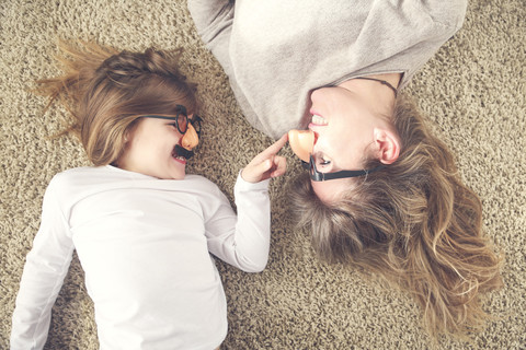 Mutter und kleine Tochter liegen auf dem Teppich und haben Spaß mit einer Comedy-Brille, lizenzfreies Stockfoto