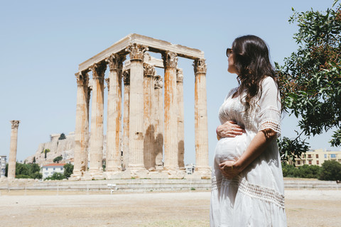 Griechenland, Athen, schwangere Frau beim Besuch des Olympieions mit der Akropolis im Hintergrund, lizenzfreies Stockfoto