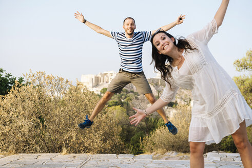 Griechenland, Athen, glückliches Paar springt auf dem Areopag mit der Akropolis und dem Parthenon im Hintergrund - GEMF01430