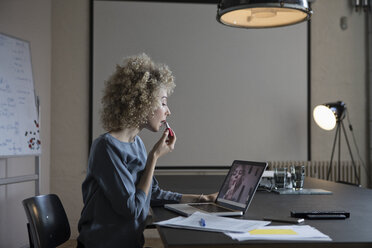 Woman in office applying make-up using laptop monitor as mirror - RBF05565