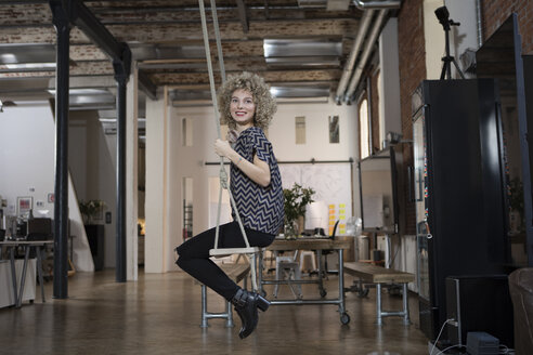 Smiling woman on swing in modern office - RBF05567