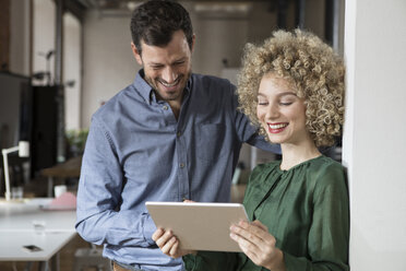 Smiling man and woman looking at tablet in office - RBF05581