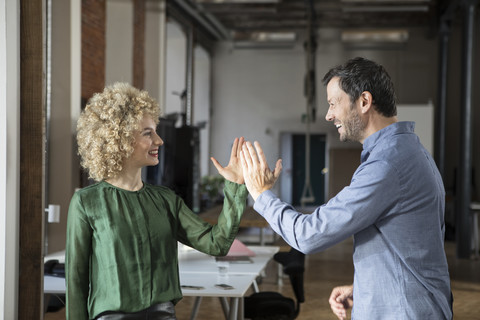 Glücklicher Mann und glückliche Frau geben sich im Büro die Hand, lizenzfreies Stockfoto