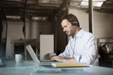 Businessman at desk with laptop and headphones - RBF05607