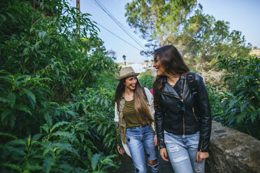 Two happy young women walking on a path with plants - KIJF01109