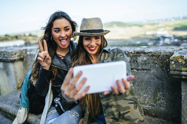 Zwei glückliche junge Frauen auf einer Reise machen ein Selfie mit einem Tablet - KIJF01115