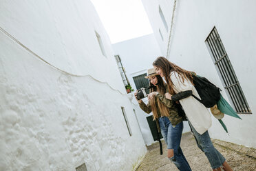 Zwei glückliche junge Frauen in einer Stadt, die sich Fotos in einer Kamera ansehen - KIJF01120