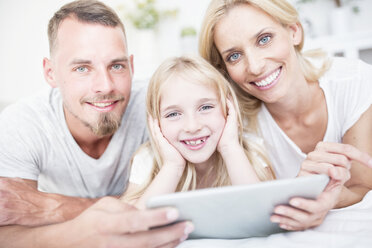 Portait of smiling girl with parents lying in bed with tablet - WESTF22533