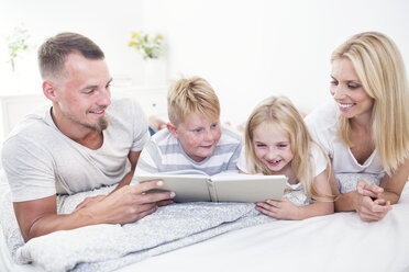 Familie liegt im Bett und liest gemeinsam ein Buch - WESTF22543