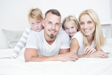 Portrait of smiling family lying in bed - WESTF22544