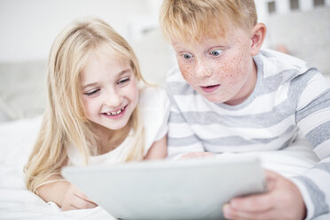 Bruder und Schwester liegen im Bett und benutzen ein Tablet - WESTF22545