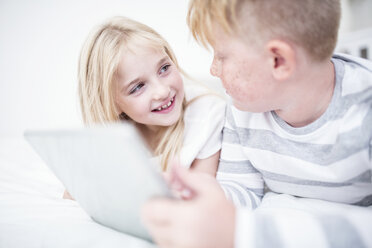 Brother and sister lying in bed using tablet - WESTF22546