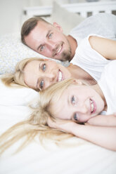 Portait of smiling girl and parents lying in bed - WESTF22551