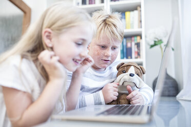 Bruder und Schwester mit Kuscheltier benutzen gemeinsam einen Laptop - WESTF22555