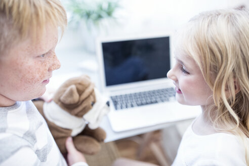 Bruder und Schwester mit Kuscheltier schauen sich vor dem Laptop an - WESTF22557