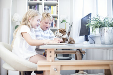 Bruder und Schwester mit Kuscheltier benutzen gemeinsam einen Laptop - WESTF22558