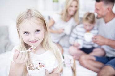 Portrait of smiling girl eating from cereal bowl with family in background - WESTF22567