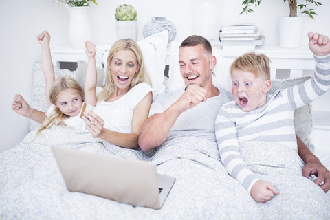 Aufgeregte Familie, die im Bett liegt und auf den Laptop schaut, lizenzfreies Stockfoto