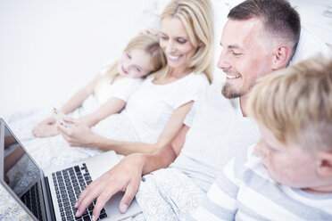 Family lying in bed using laptop - WESTF22572