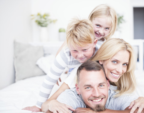 Porträt einer lächelnden Familie, die übereinander im Bett liegt, lizenzfreies Stockfoto