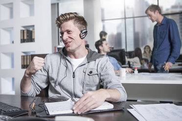 Young man at desk in office wearing a headset - ZEF12495