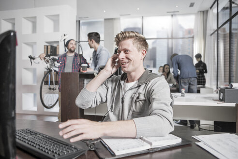 Junger Mann am Schreibtisch im Büro mit einem Headset - ZEF12497