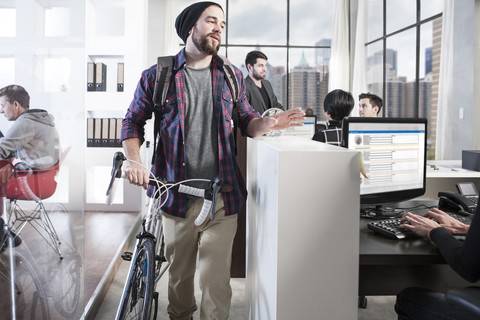 Lässiger Mann mit Fahrrad in modernem Büro, lizenzfreies Stockfoto