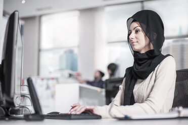 Junge Frau mit Hidschab bei der Arbeit am Schreibtisch im Büro - ZEF12536