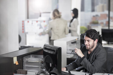 Smiling businessman working on computer in office - ZEF12541