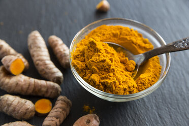 Glass bowl of curcuma powder and fresh organic curcuma on slate - SARF03134