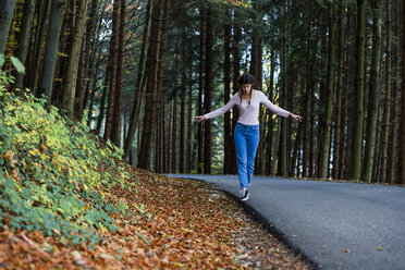 Junge Frau balanciert am Straßenrand im Wald - WVF00823