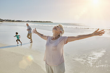 Happy senior woman standing on the beach with arms outstretched - RORF00537