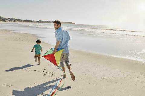 Vater und kleiner Sohn spielen mit Drachen am Strand, lizenzfreies Stockfoto