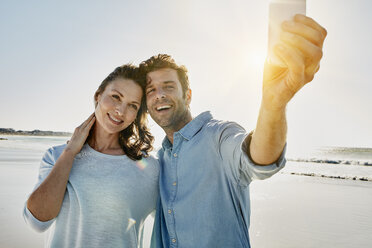 Porträt eines glücklichen Paares, das mit seinem Smartphone ein Selfie am Strand macht - RORF00569