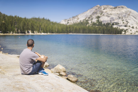 USA, Kalifornien, Yosemite National Park, Mann sitzt an einem Bergsee, lizenzfreies Stockfoto