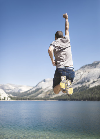USA, Kalifornien, Yosemite-Nationalpark, Rückansicht eines Mannes, der an einem Bergsee in die Luft springt, lizenzfreies Stockfoto