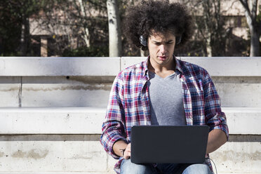 Young man using laptop and headphones - ABZF01796