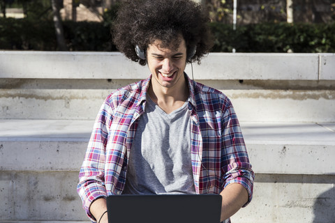 Lächelnder junger Mann mit Laptop und Kopfhörern, lizenzfreies Stockfoto