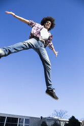 Lächelnder junger Mann, der mit ausgestreckten Armen in die Luft springt - ABZF01804
