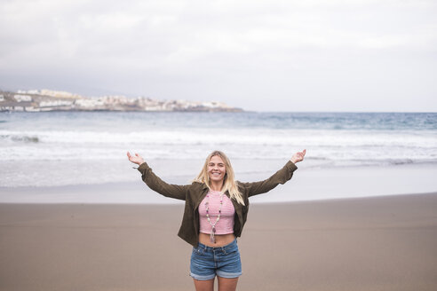Porträt einer glücklichen jungen Frau, die mit ausgestreckten Armen am Strand steht - SIPF01350