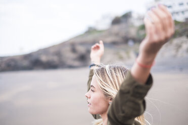 Blonde junge Frau steht mit ausgestreckten Armen am Strand und schaut in die Ferne - SIPF01352