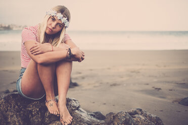 Porträt einer jungen Frau mit Blumen auf einem Felsen am Strand sitzend - SIPF01355