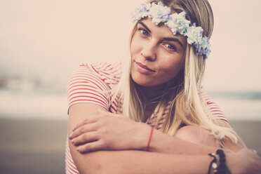 Portrait of young woman wearing flowers sitting on the beach - SIPF01356