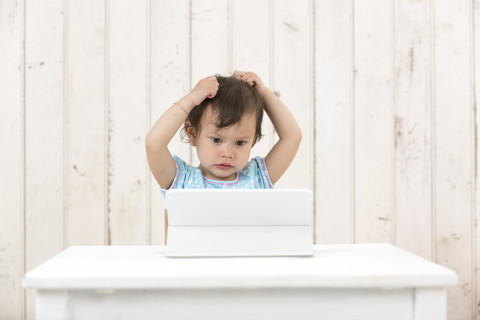 Porträt eines kleinen Mädchens, das sich die Haare rauft, während es auf einen Laptop schaut, lizenzfreies Stockfoto