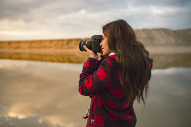 Junge Frau fotografiert am Strand mit Kamera bei Sonnenuntergang - RAEF01689