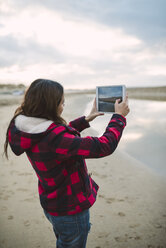 Junge Frau fotografiert mit Tablet am Strand - RAEF01693